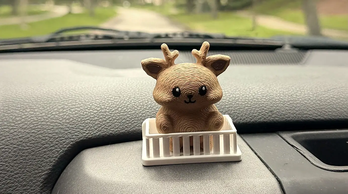 The printed Mofflits Deer sitting inside its small white fence-style car mount on a real truck dashboard, trees and road blurred behind